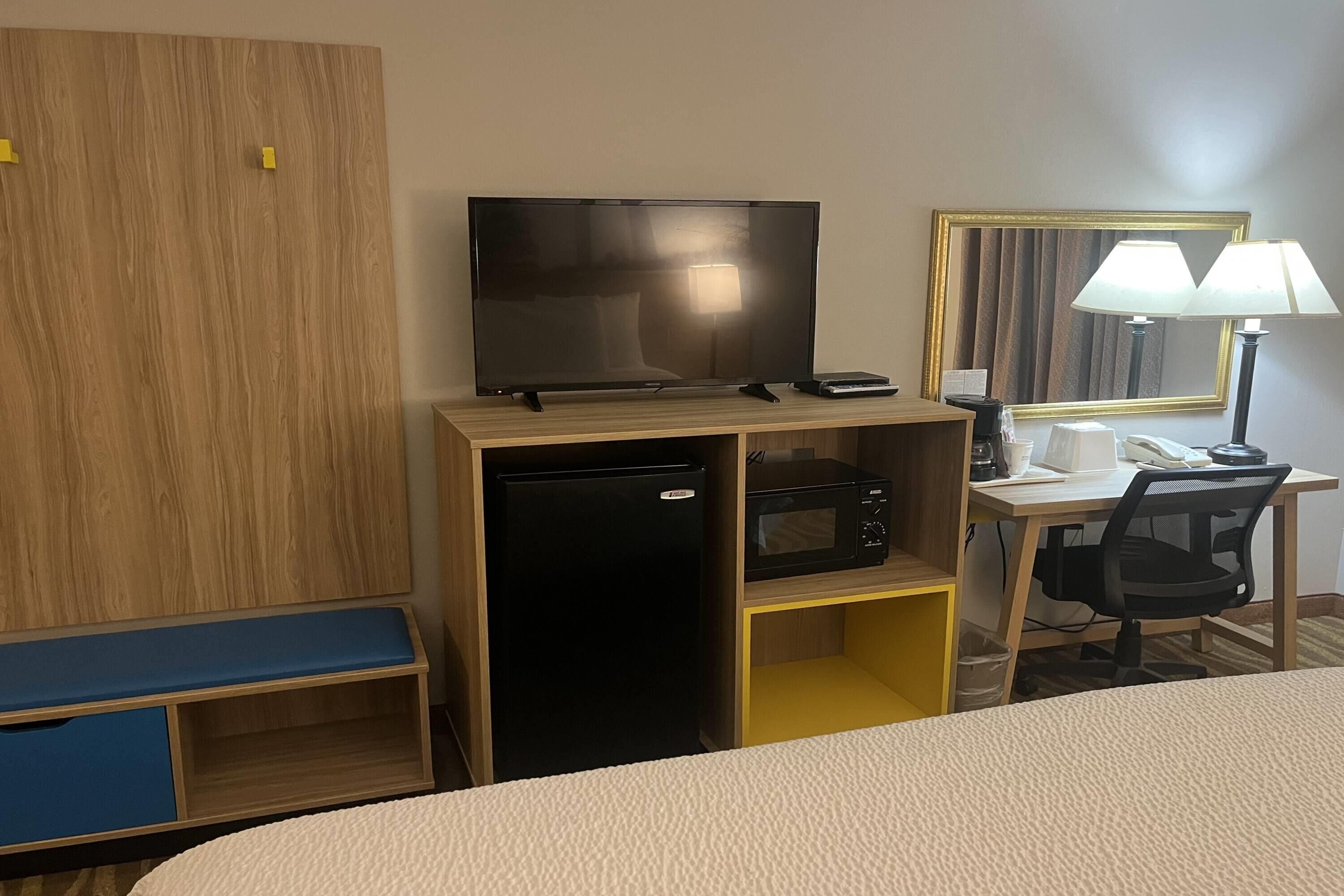Een hotelkamer met een bed, een bureau met computer, een televisie, een magnetron en een kleine koelkast.