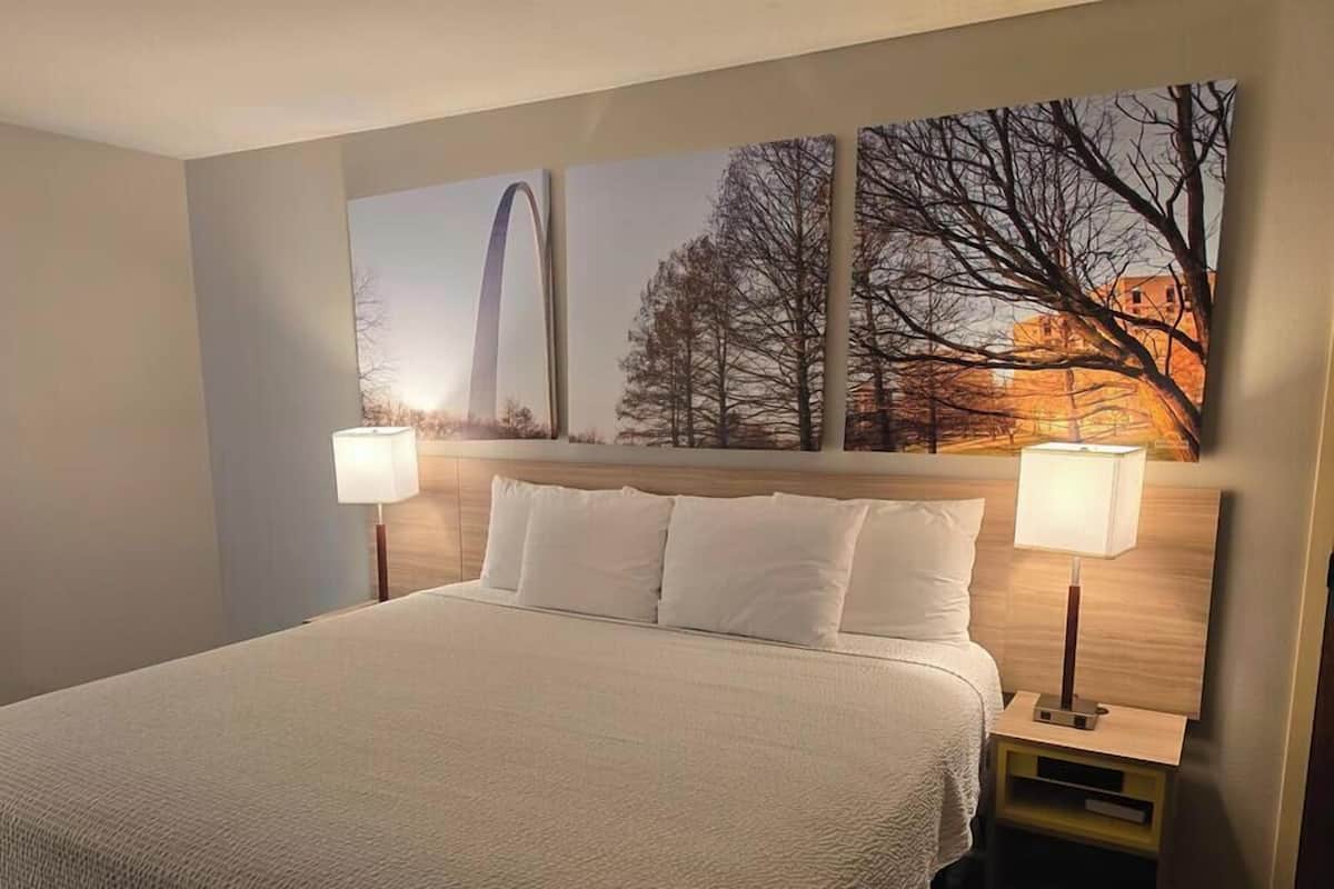 Ein Hotelzimmer mit einem großen Bett, zwei Nachttischlampen, einem Nachttisch und einer Wand mit drei gerahmten Bildern.