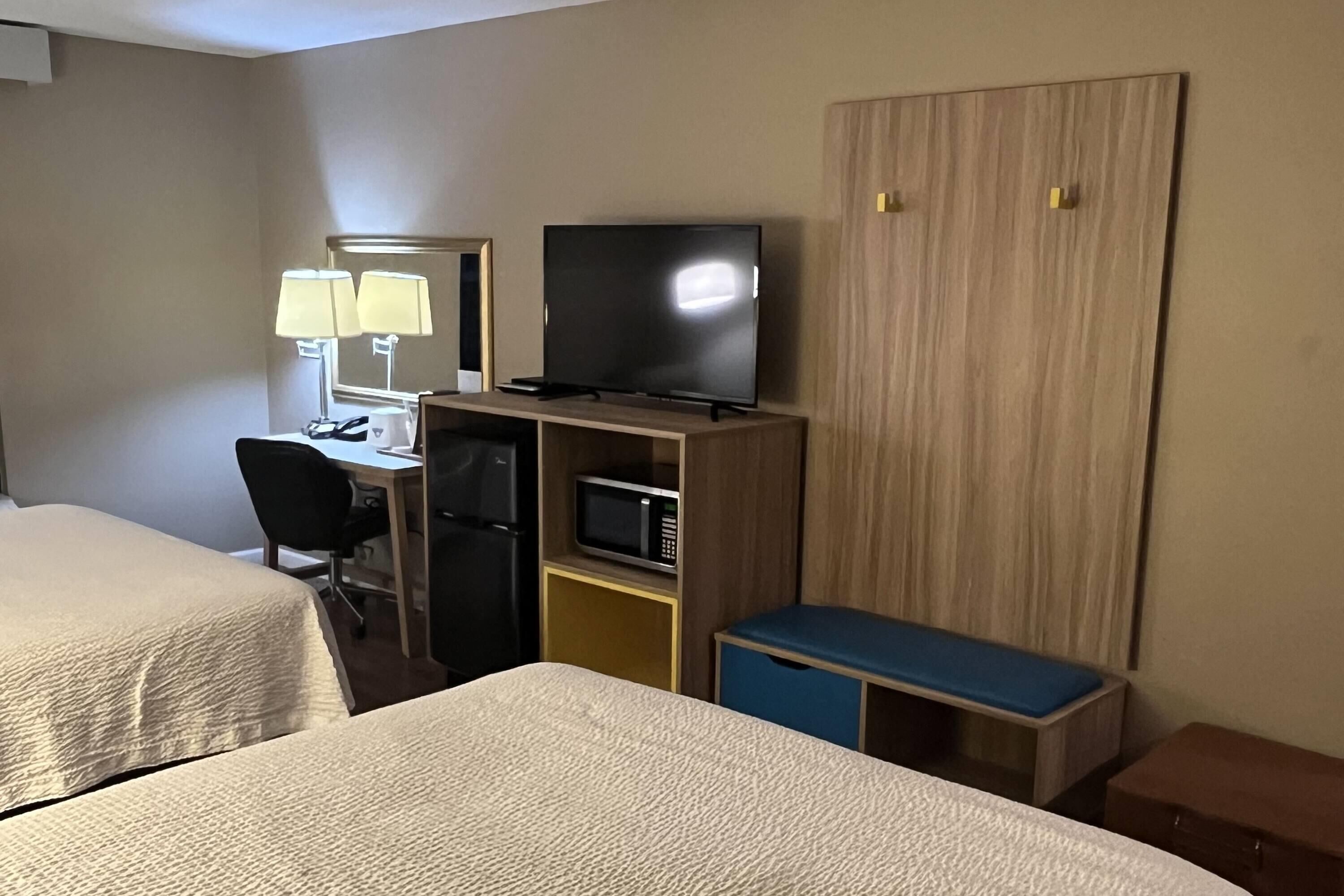 A hotel room with two beds, a desk with a computer, a television, a microwave, and a wardrobe.