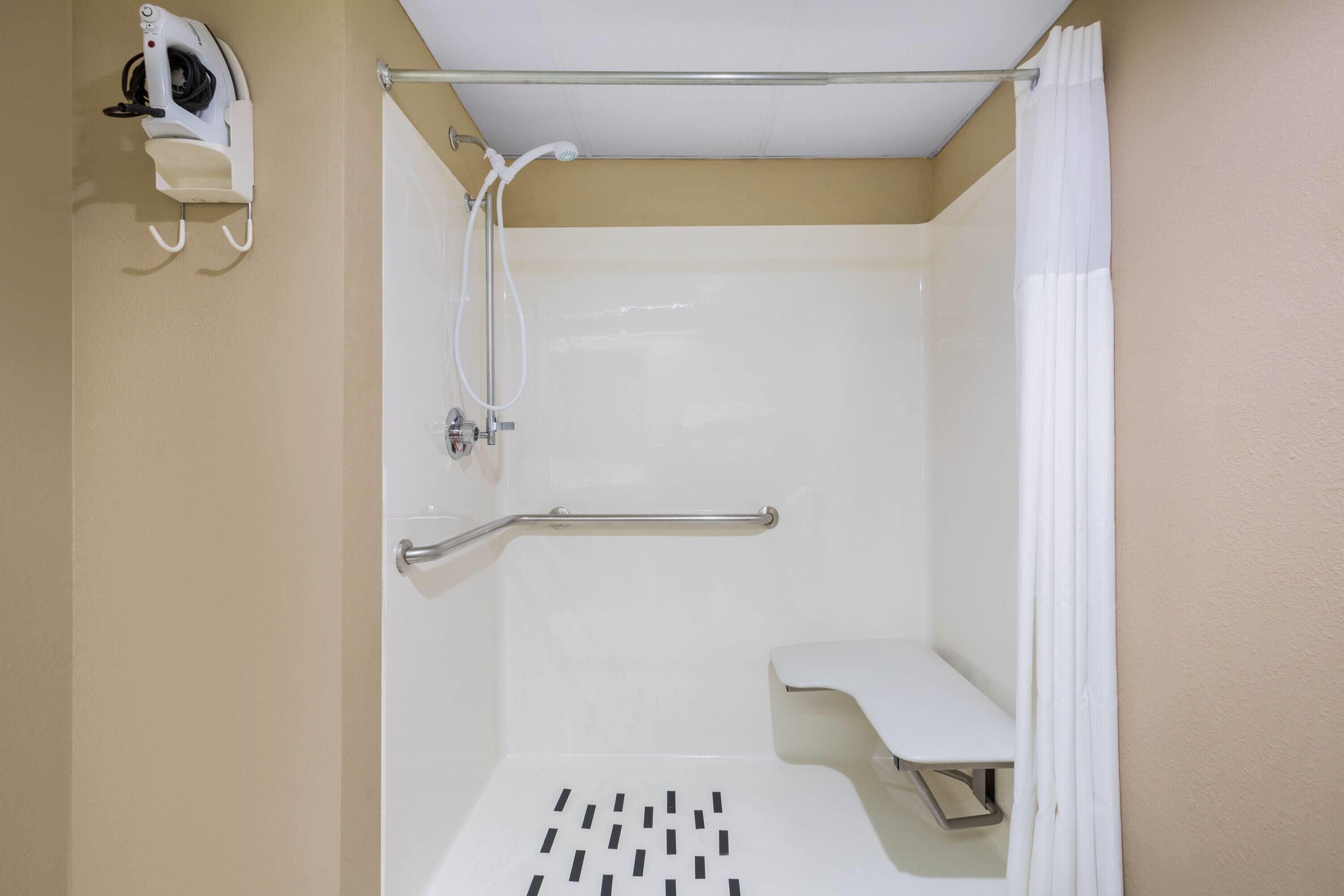 Ducha con barra de apoyo, banco blanco y cabezal de ducha manual.