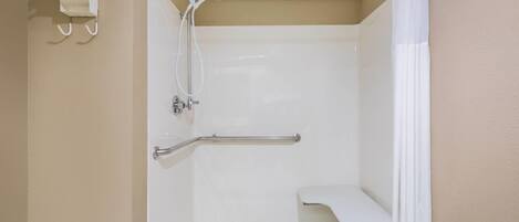 Ducha con barra de apoyo, banco blanco y cabezal de ducha manual.