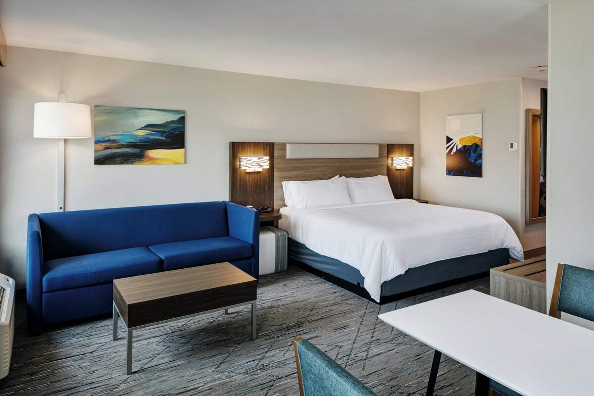 Une chambre d’hôtel avec un lit, un canapé bleu, une petite table et une lampe.