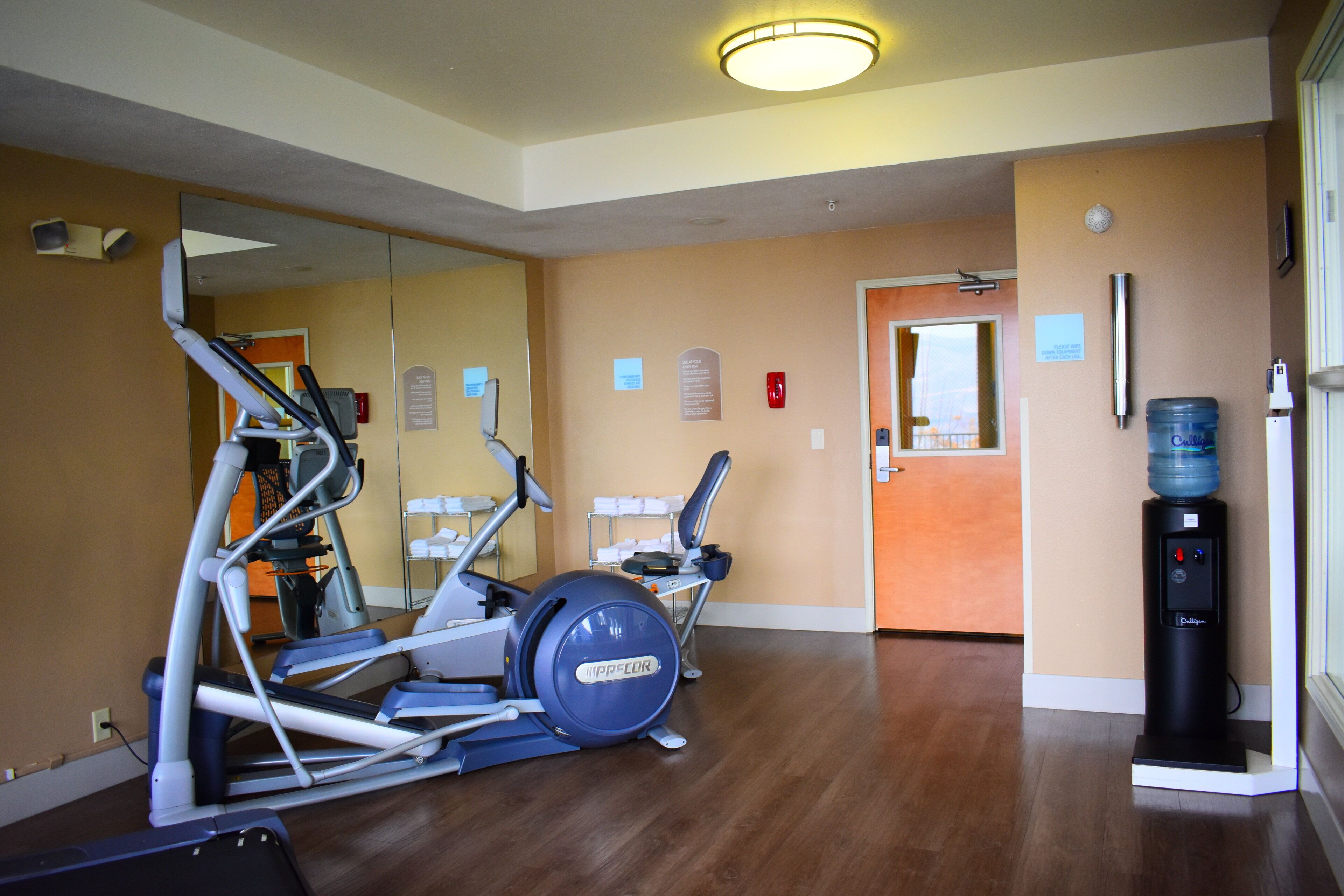 Un gimnasio con equipamiento de ejercicio, dispensador de agua y un espejo.