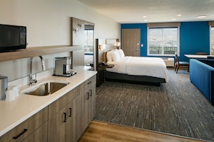 Una habitación de hotel moderna con kitchenette, una cama, un escritorio y vistas al exterior.