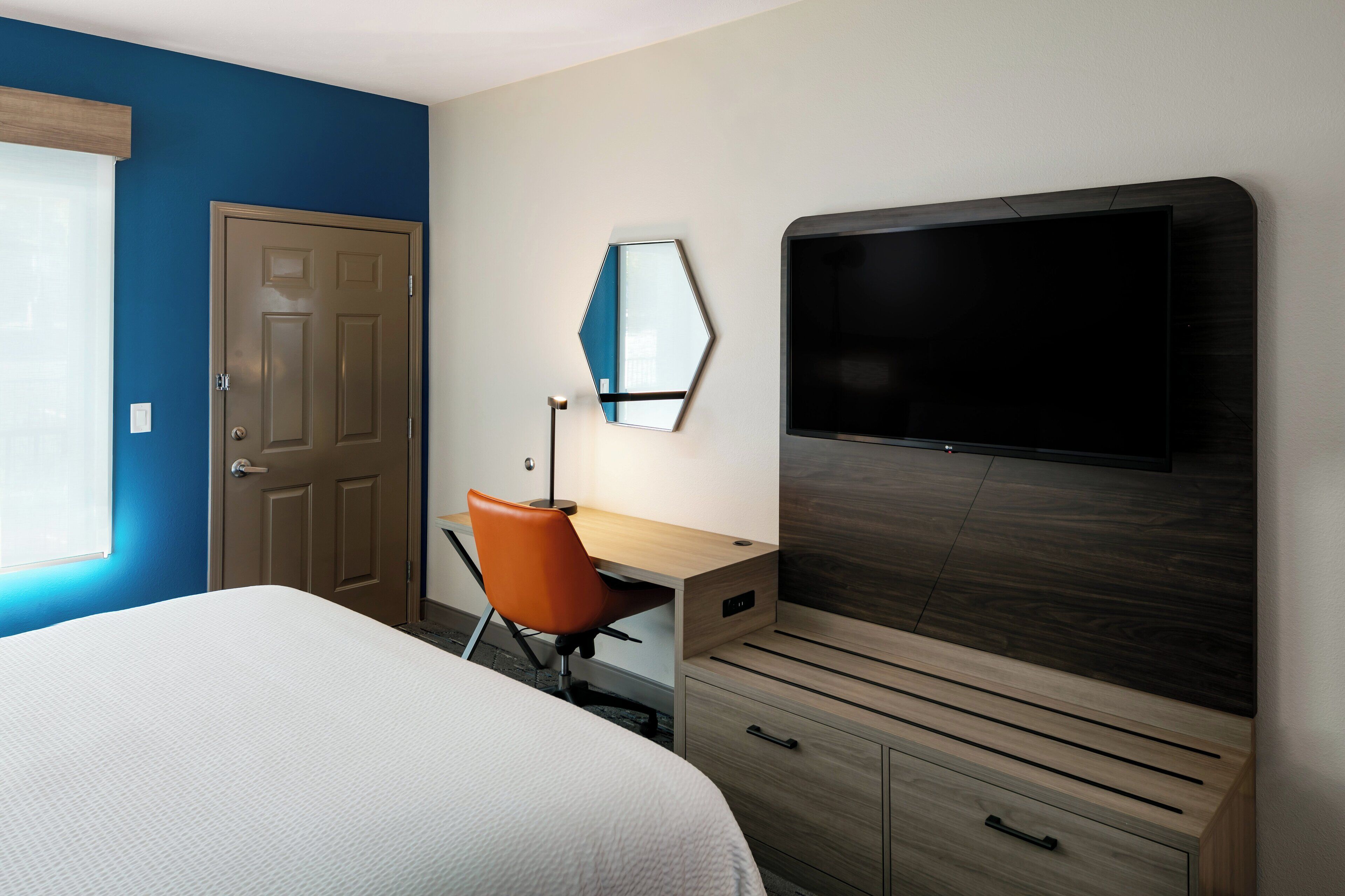 A hotel room with a bed, a desk, a chair, a TV, and a wardrobe.