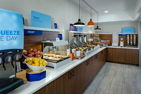 Un buffet de petit-déjeuner avec des présentoirs indiquant les différents types de produits proposés : fruits, céréales, et une machine à café.