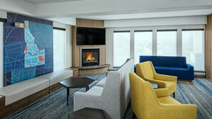A modern hotel room with a fireplace, a large wall map, a blue sofa, and a yellow armchair.