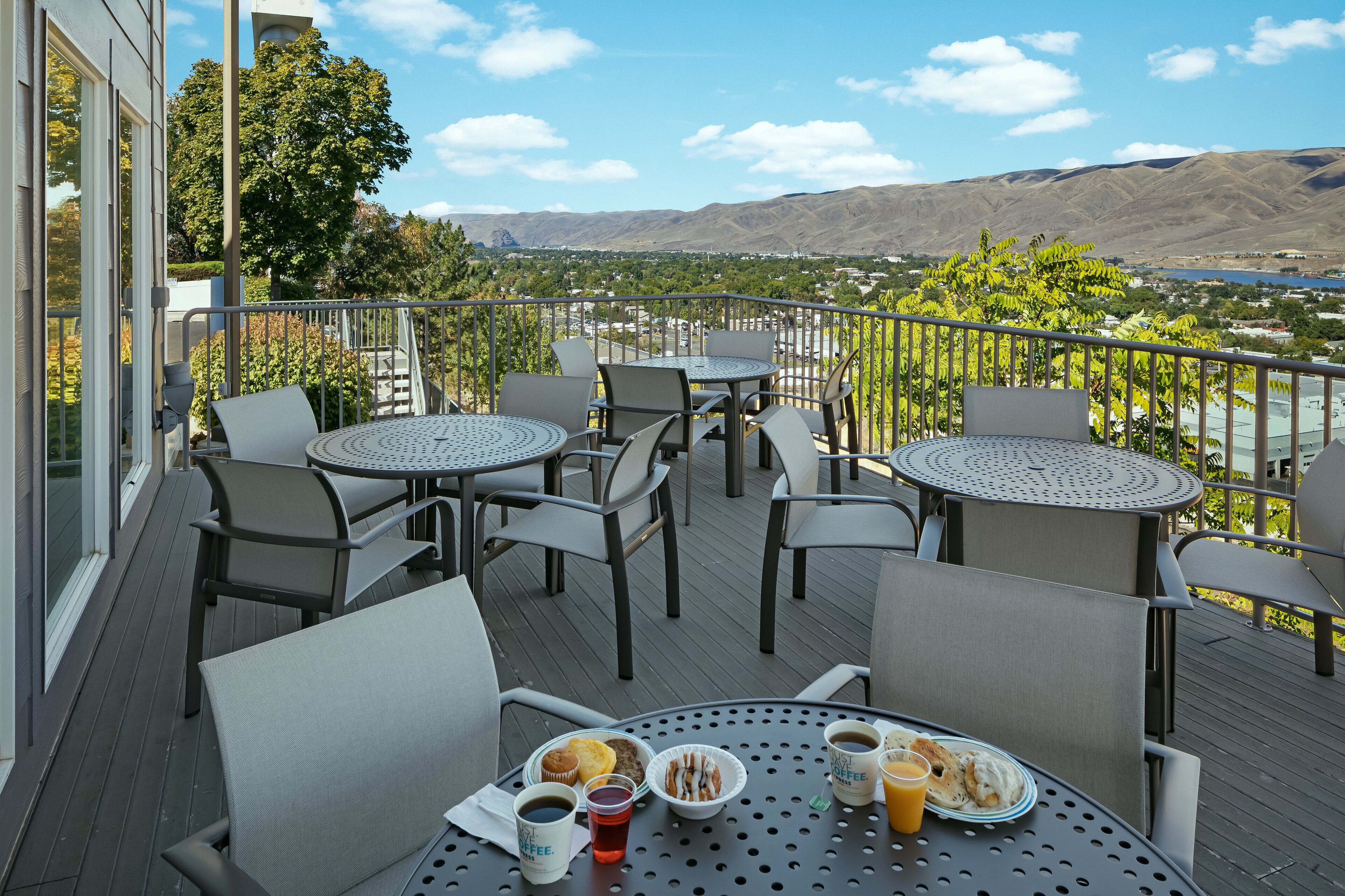 A deck with round tables and chairs, a table with breakfast items, and a scenic view of mountains and a lake.