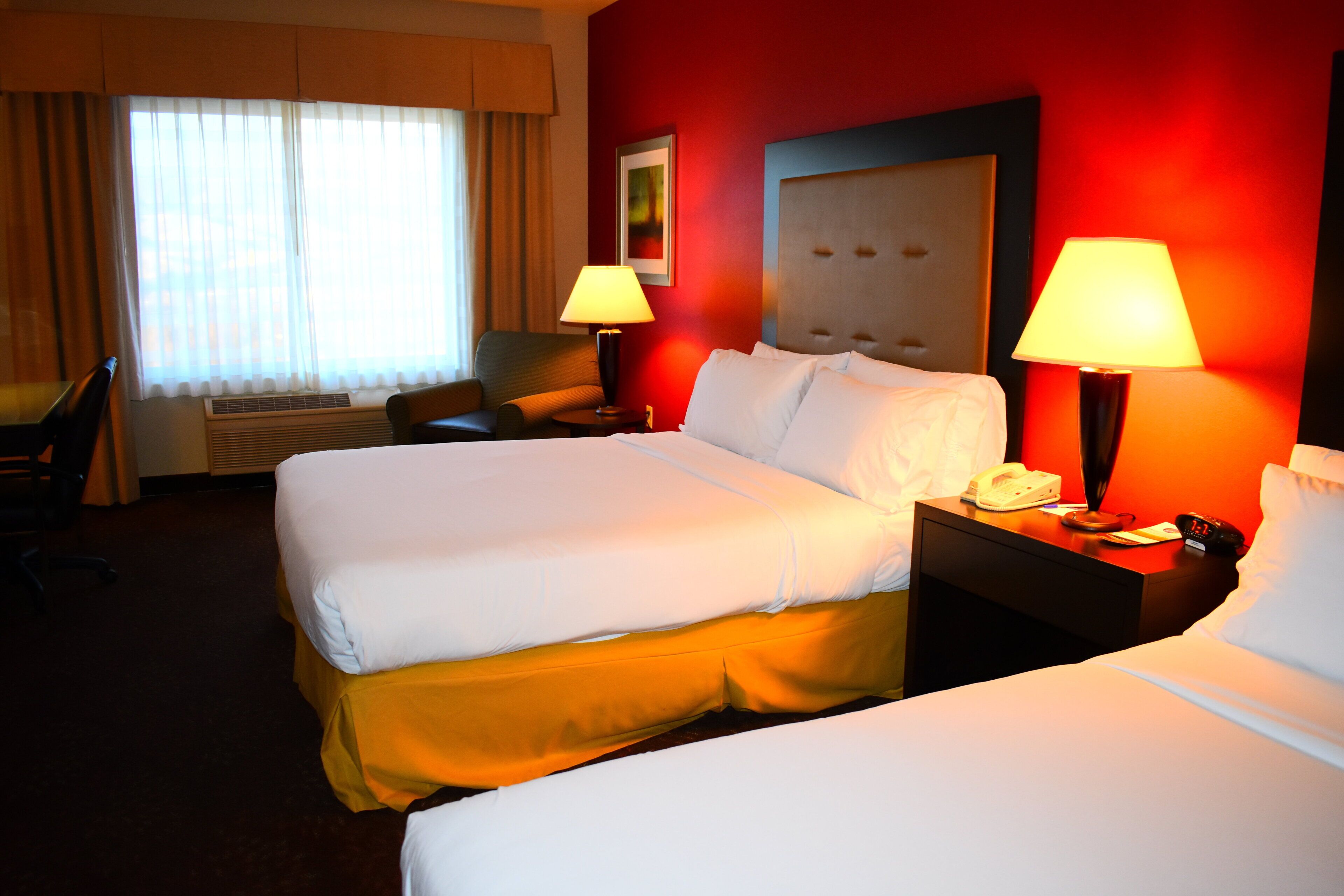A hotel room with two beds, a desk, and a chair. There are two lamps on the nightstands.