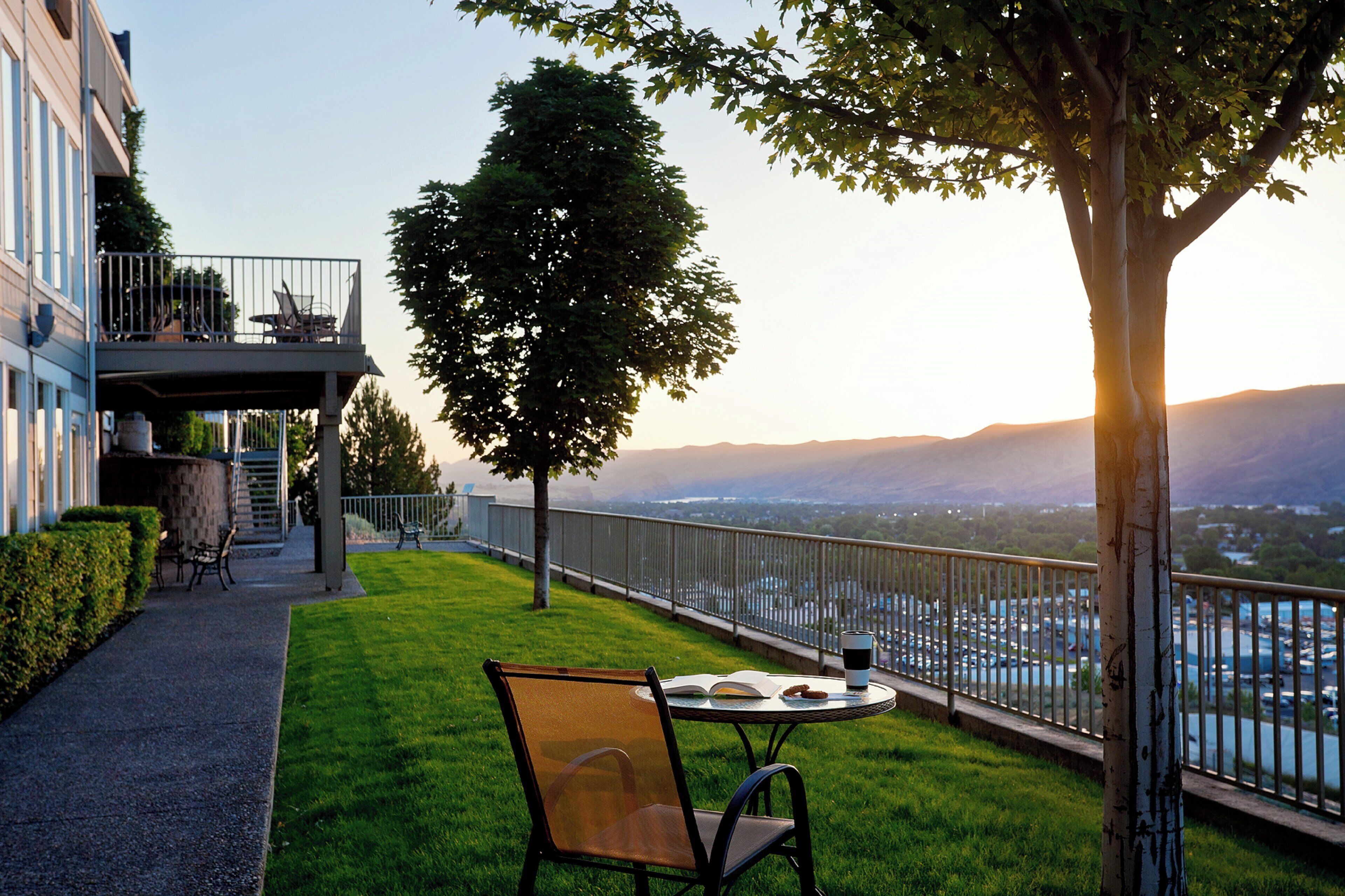 A balcony with a table and chairs, overlooking a body of water and distant mountains.