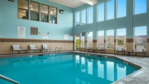 An indoor swimming pool with clear blue water, surrounded by beige and blue walls, and a view of a desert landscape through large windows.