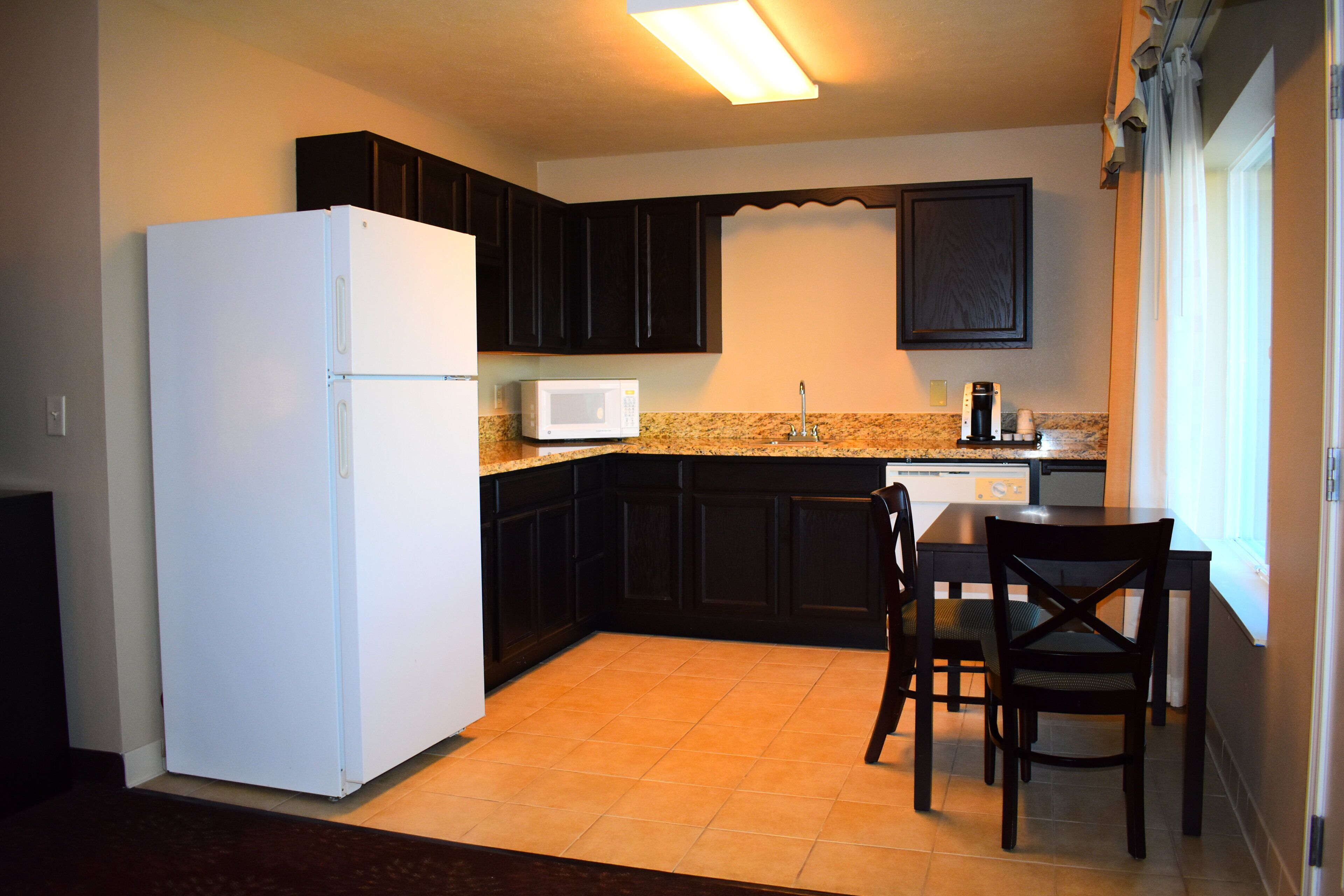 Una cocina compacta con armarios oscuros, un refrigerador blanco, un microondas y una cafetera.