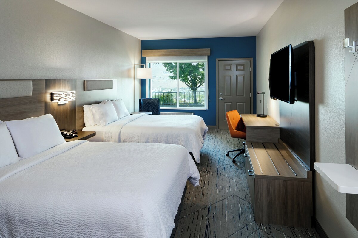 Une chambre d’hôtel avec deux lits, un bureau, une télévision et une fenêtre donnant sur des arbres.