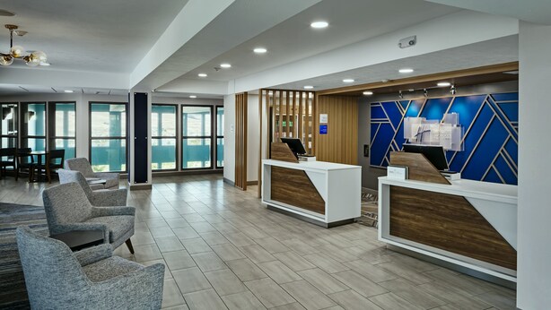 A modern reception area with a wooden reception desk, grey upholstered chairs, and large windows providing natural light.