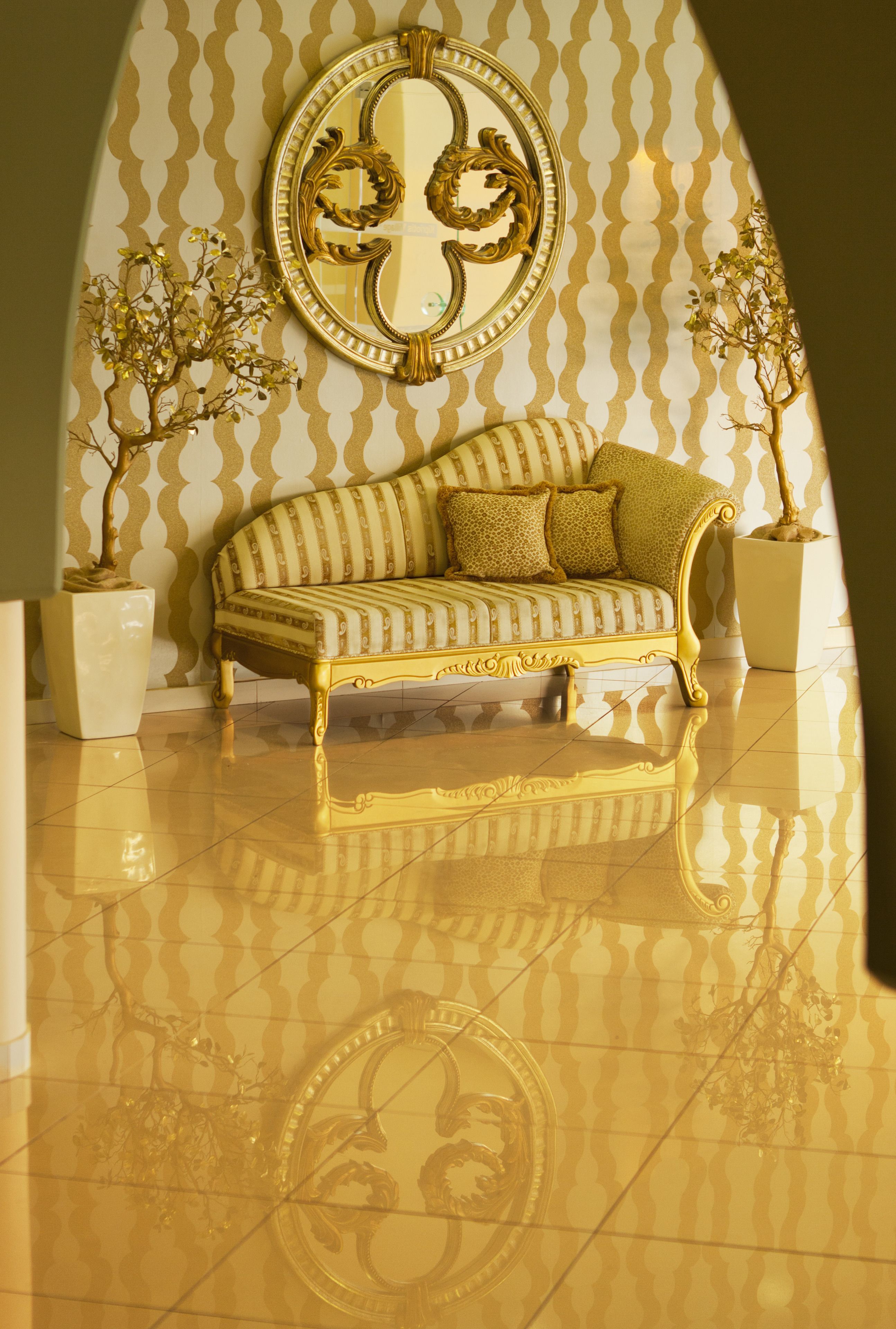 Una habitación con un sofá de marco dorado, un espejo grande con marco decorativo y dos plantas en macetas.