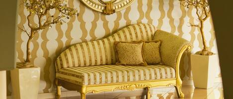 Una habitación con un sofá de marco dorado, un espejo grande con marco decorativo y dos plantas en macetas.