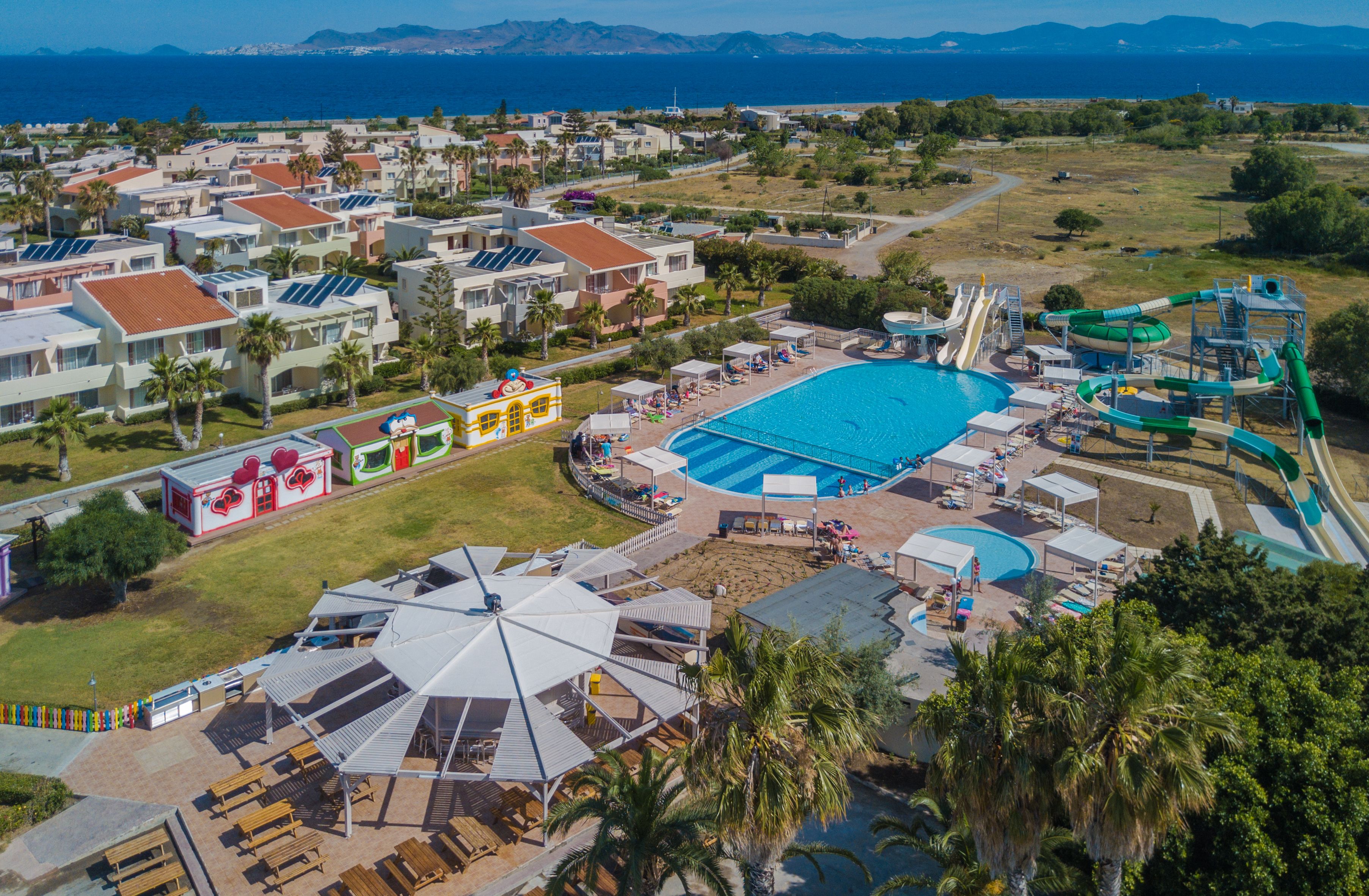 An aerial view of a resort with a large swimming pool, water slides, and a beach area.