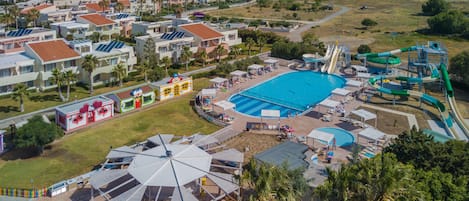 An aerial view of a resort with a large swimming pool, water slides, and a beach area.