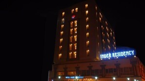Un hotel llamado 'INDER RESIDENCY', con varios pisos y ventanas iluminadas durante la noche.