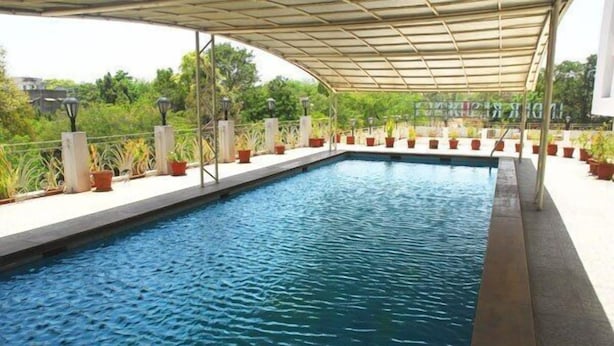 Una piscina con zona cubierta, rodeada de plantas en macetas y una barandilla metálica.