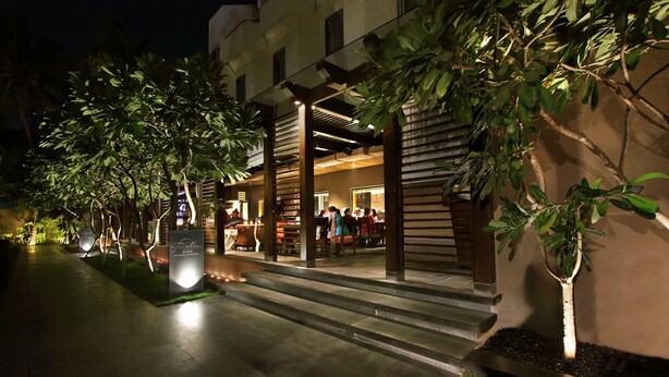 An outdoor dining area with tables and chairs, surrounded by trees and a building with a modern design. - Hotel Express Residency (Vadodara)