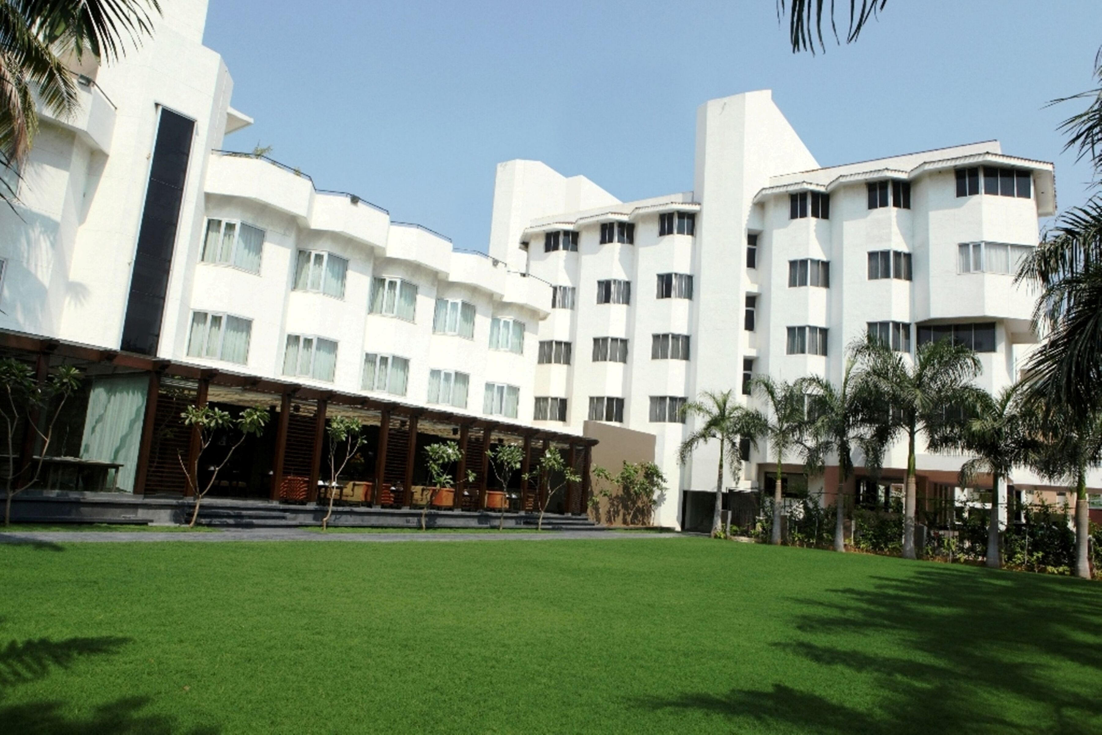 A modern hotel with a covered outdoor seating area, multiple floors, and a well-maintained lawn.