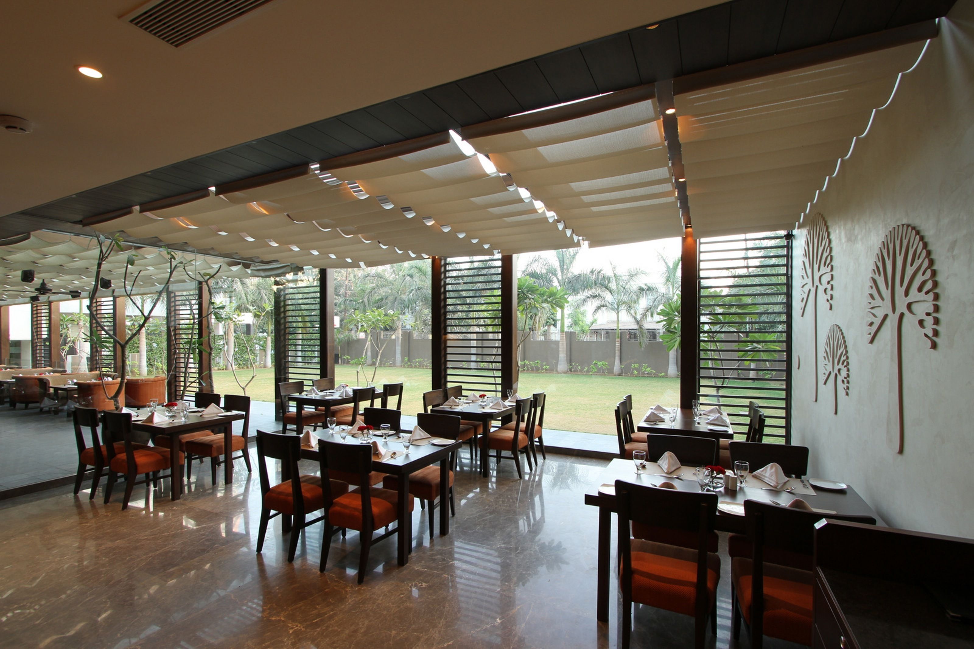 Un comedor amplio con varias mesas y sillas, ventanas grandes que ofrecen vistas al exterior e iluminación empotrada en el techo.