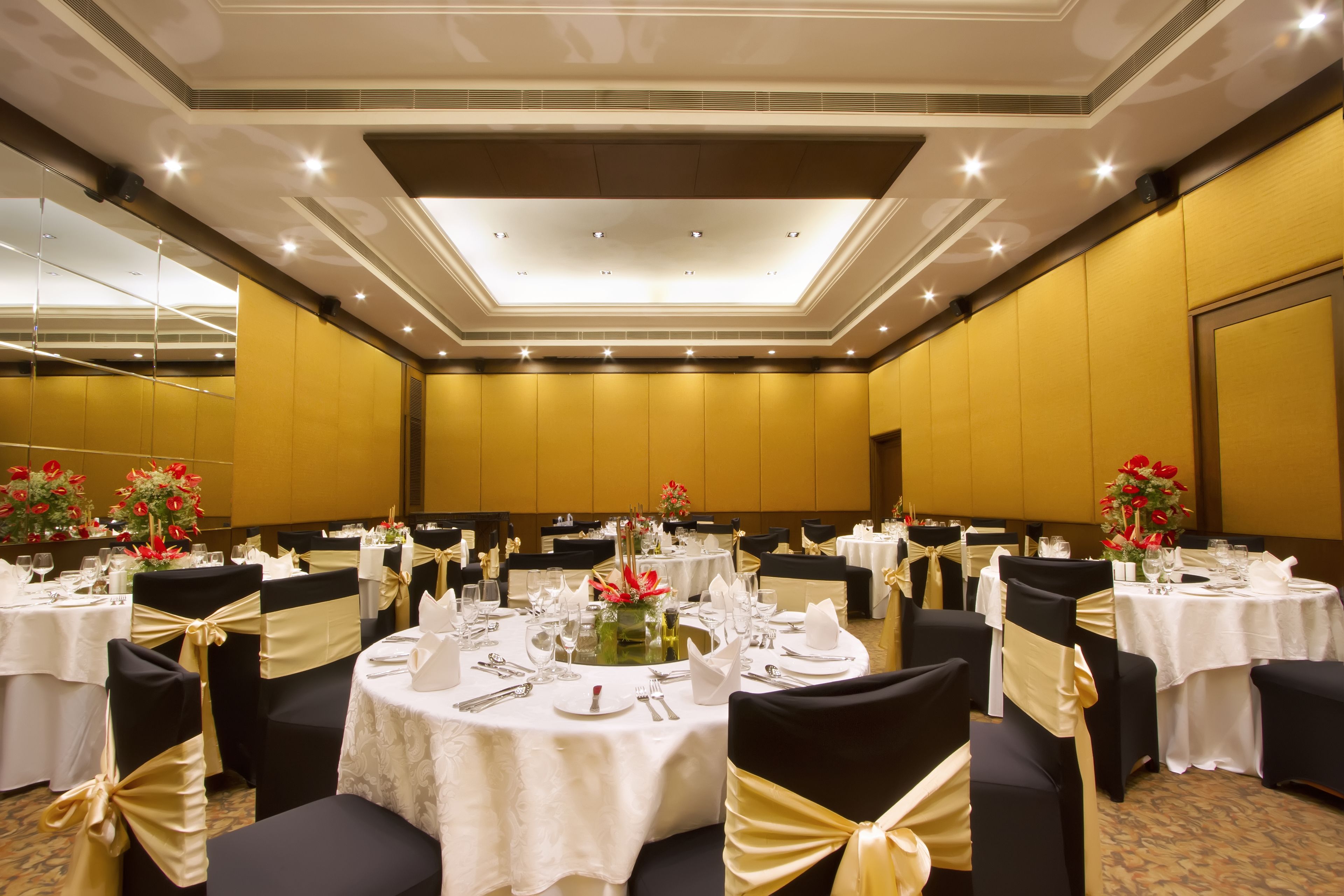 A banquet hall with round tables, black chairs with gold sashes, and white tablecloths.