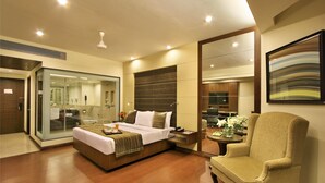 A modern hotel room with a large bed, a sitting area with a chair, a small table, and a large mirror. - Hotel Express Residency (Vadodara)