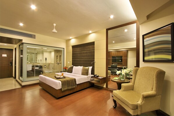 A modern hotel room with a large bed, a sitting area with a chair, a small table, and a large mirror.