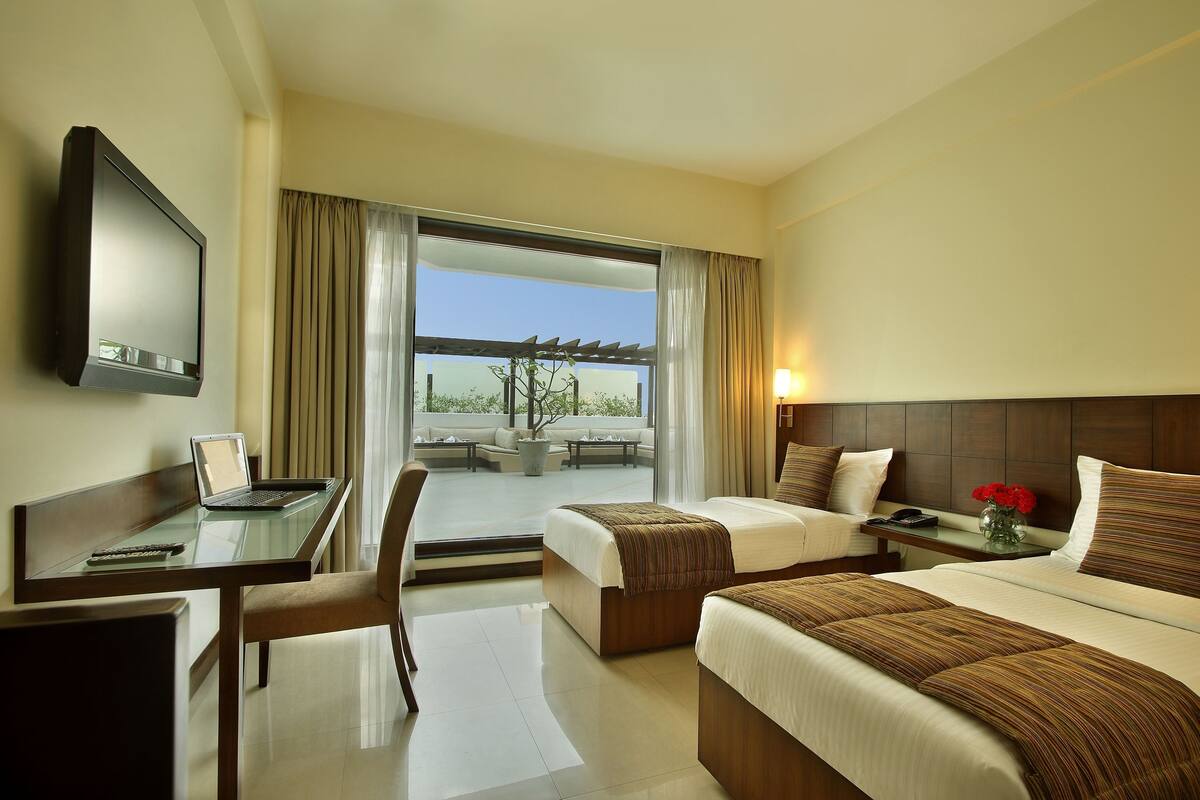 A hotel room with a bed, a desk with a laptop, a TV, and a view of the outdoors.