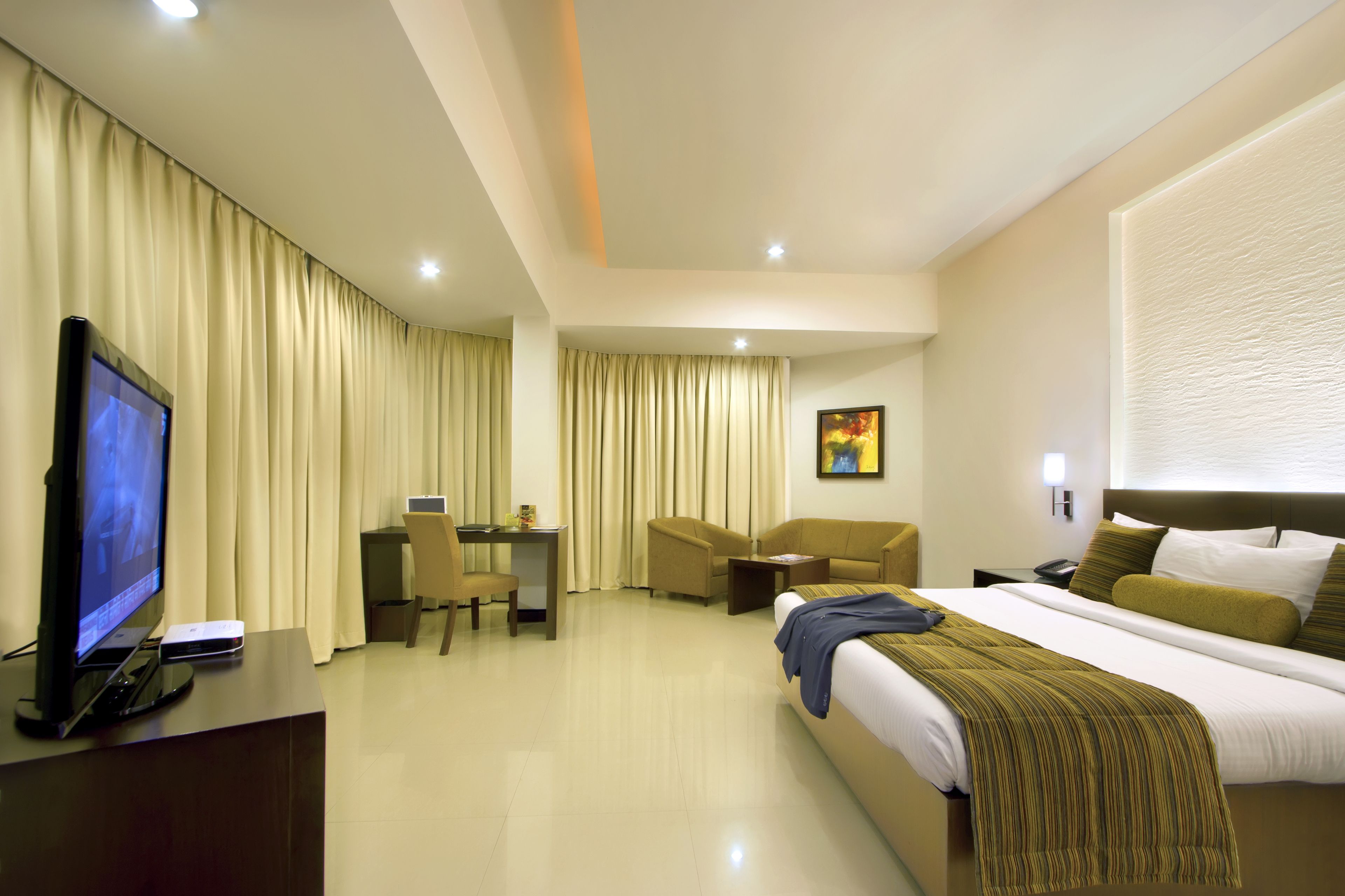 A hotel room with a bed, a desk, a chair, a TV, and a painting on the wall.