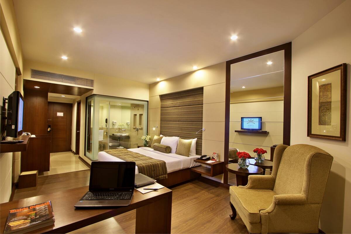 A hotel room with a bed, a desk with a laptop, a chair, a TV, and a mirror.