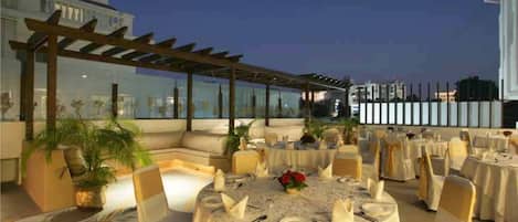 An outdoor dining area with round tables, chairs, and a pergola structure.
