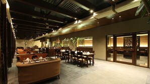 A spacious restaurant with high ceilings, modern lighting, and a mix of seating areas including a long communal table and individual booths. - Hotel Express Residency (Vadodara)