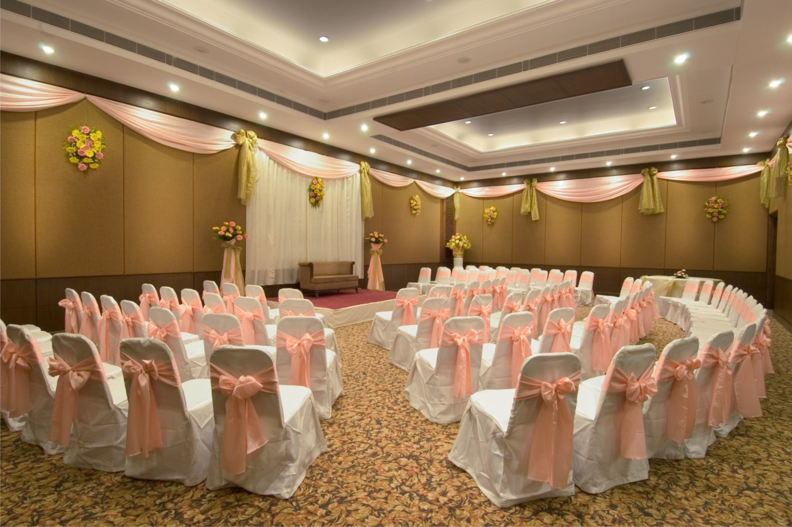 A conference room with rows of white chairs with pink sashes, a stage with a podium, and floral decorations on the walls.