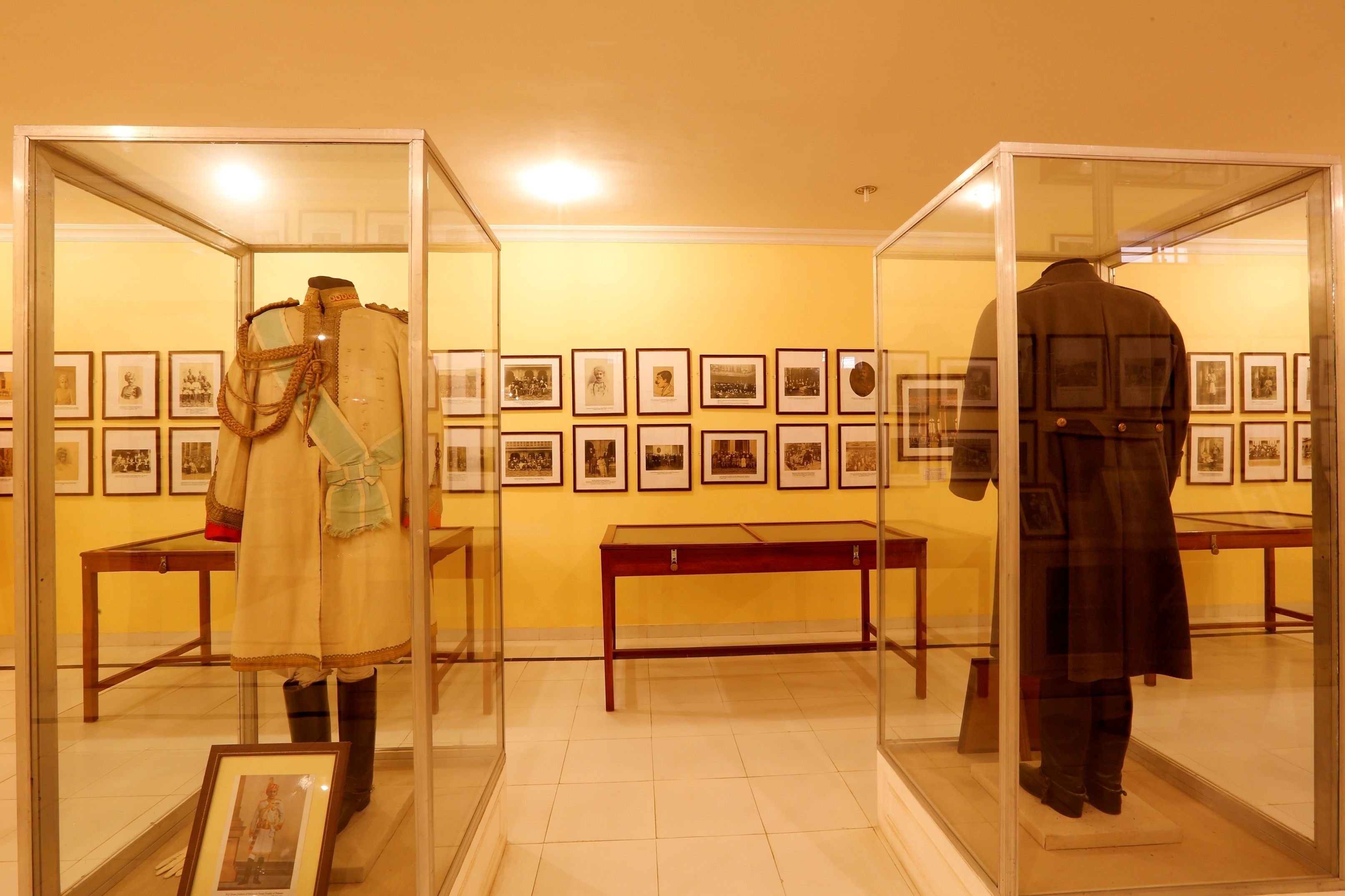 Two mannequins in glass display cases, each dressed in historical military uniforms, with framed pictures on the wall behind them.