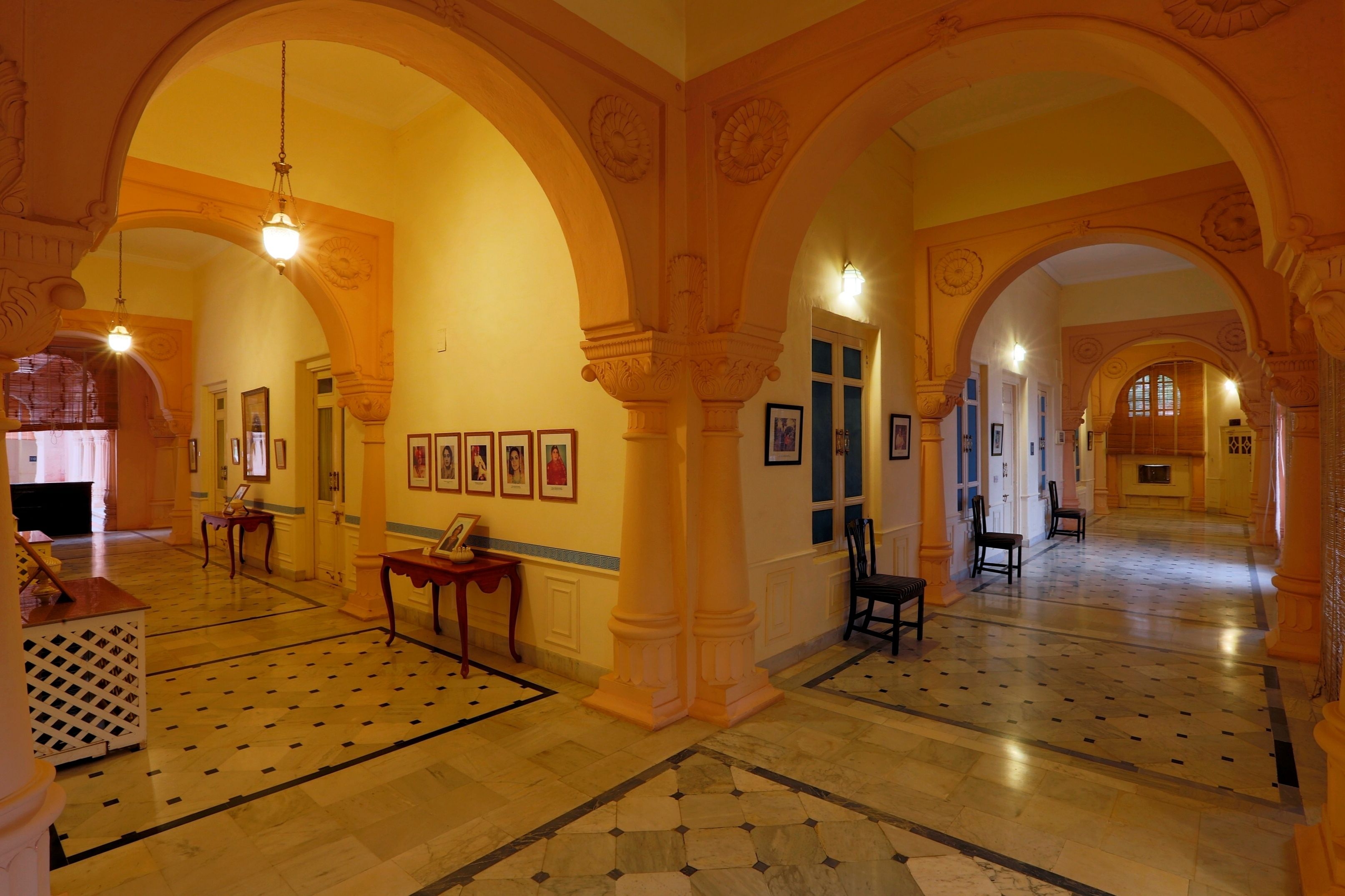 A grand hallway with ornate arches, a patterned floor, and framed pictures on the walls.