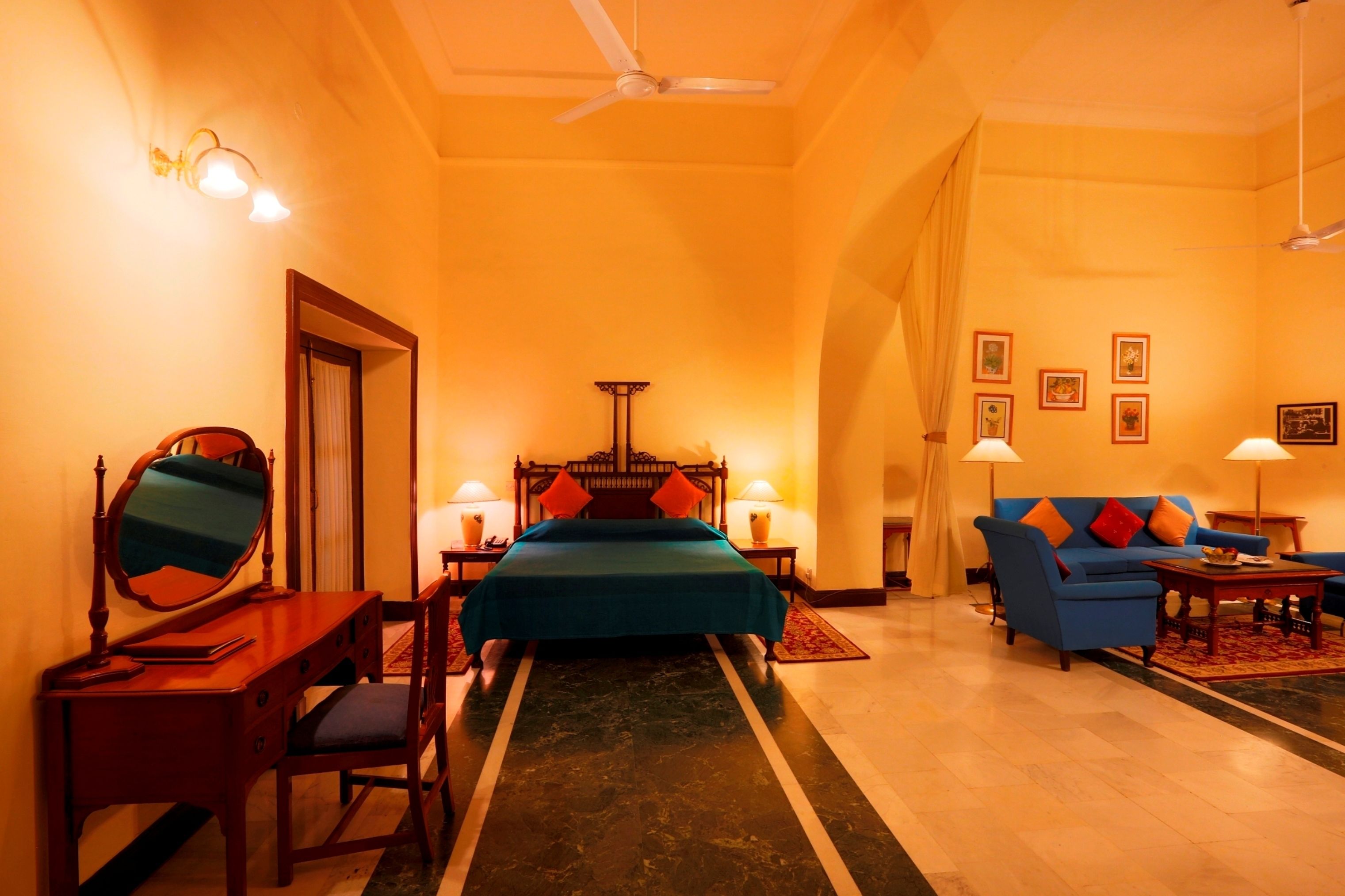 A hotel room with a bed, a desk with a mirror, a chair, a sofa, and two lamps.