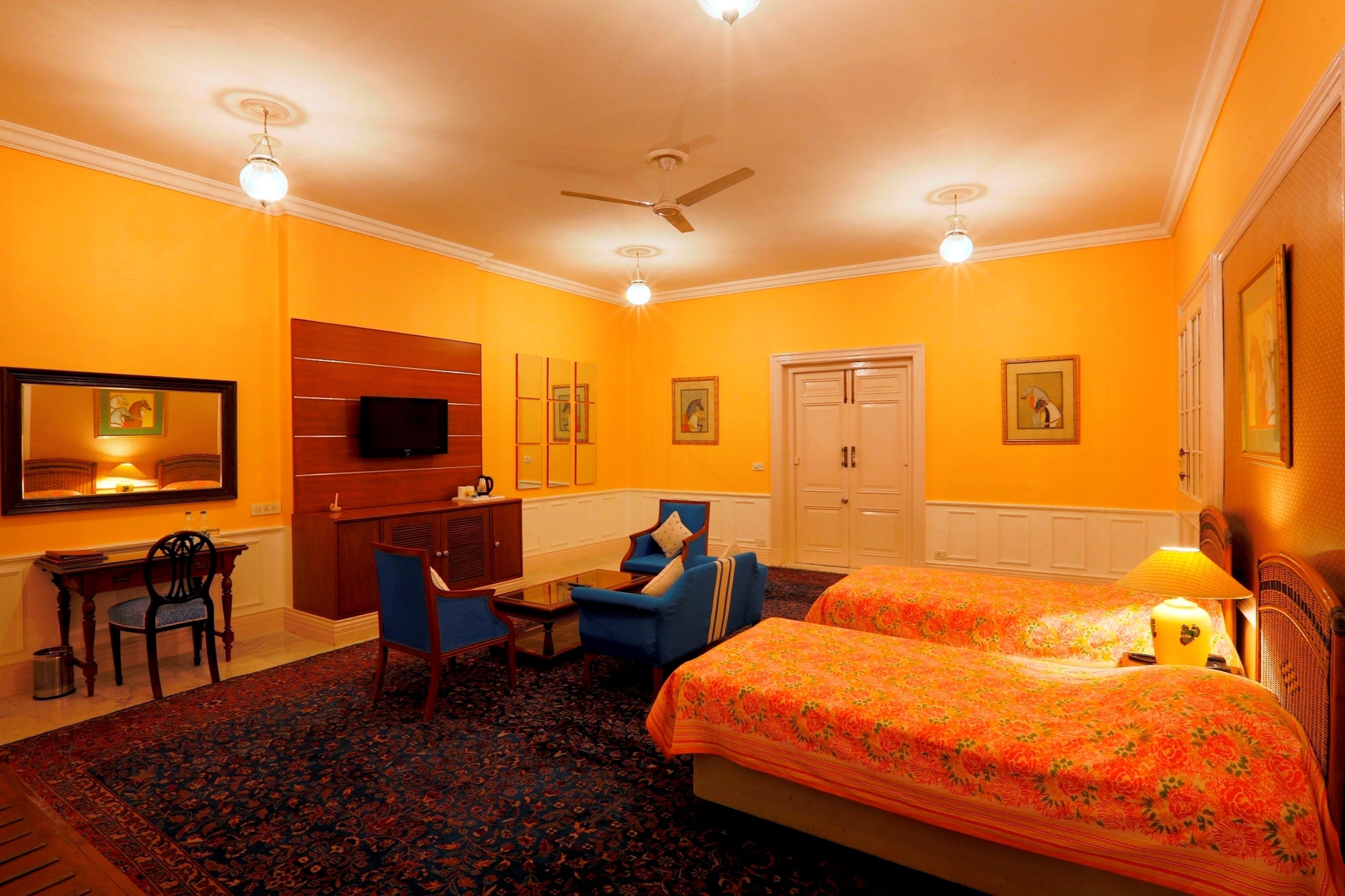 A hotel room with two beds, a desk, a chair, a television, and a ceiling fan.