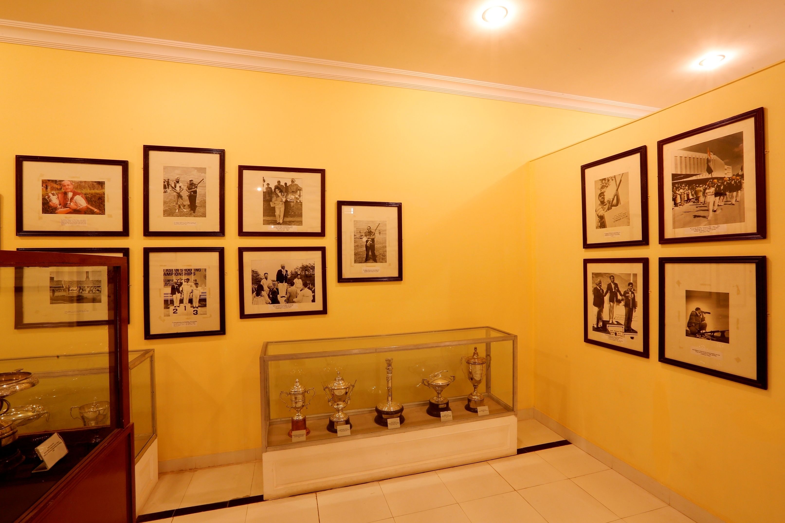 A hallway with framed photographs on the walls and a display case with trophies.