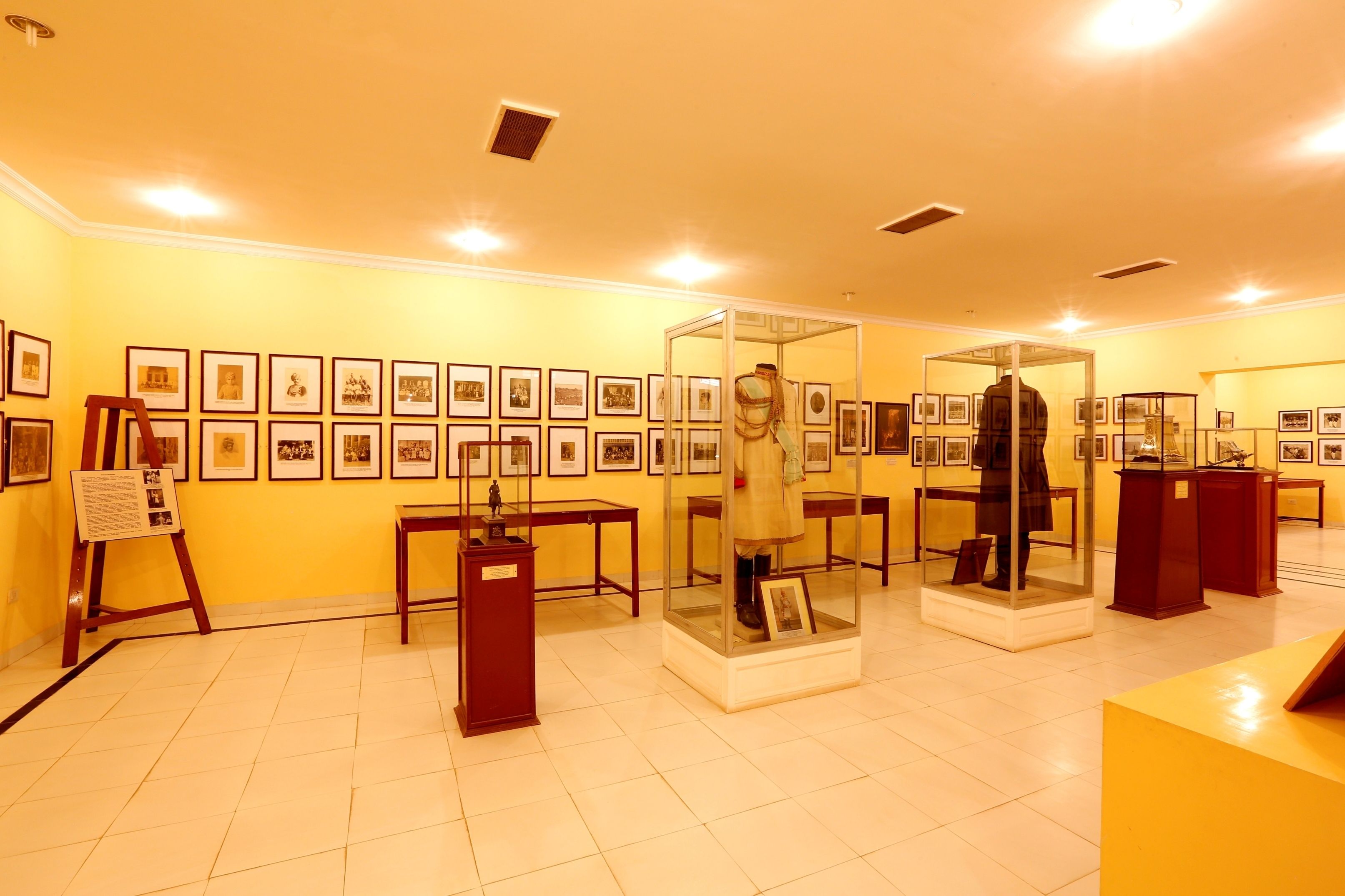 Une galerie d’art avec des tableaux encadrés accrochés aux murs, des vitrines et des tables en bois.