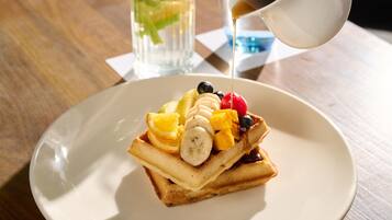 A plate with a stack of pancakes topped with fruit and syrup, a glass of water, and a cup of coffee on a wooden table.