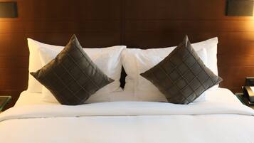 A neatly made bed with two large square pillows, a dark brown quilted headboard, and three framed artworks above the bed.