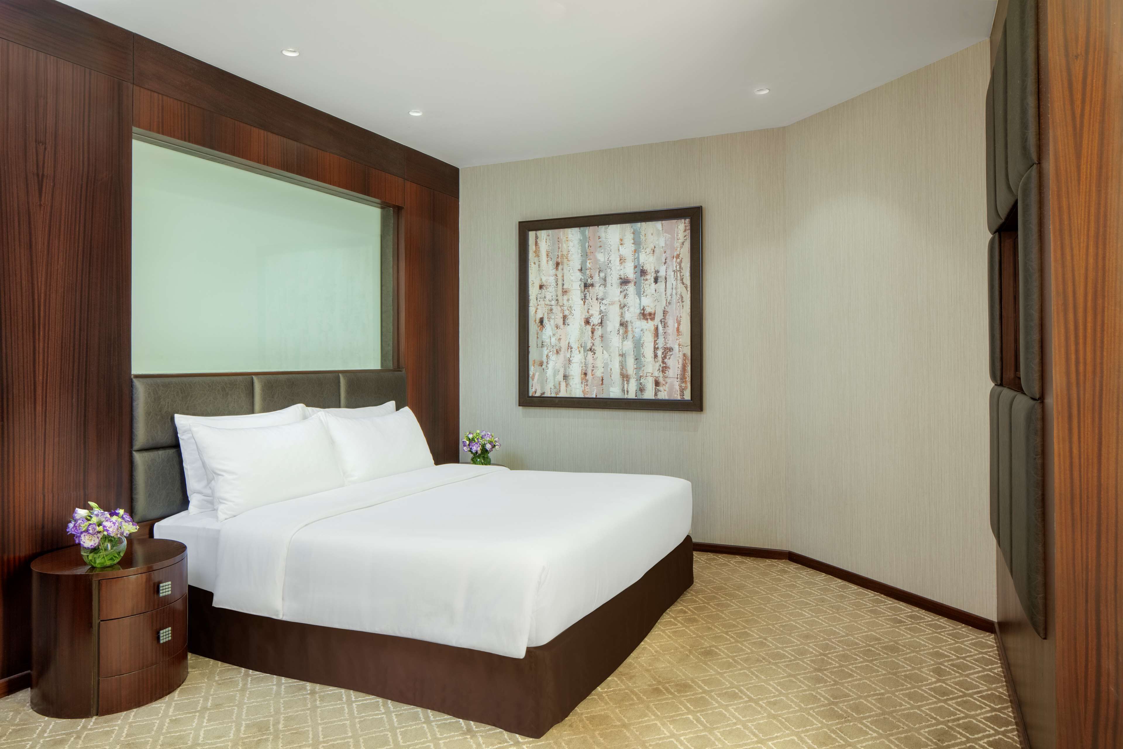 Habitación de hotel con una cama grande, una mesita de noche, un cuadro enmarcado en la pared y una ventana.