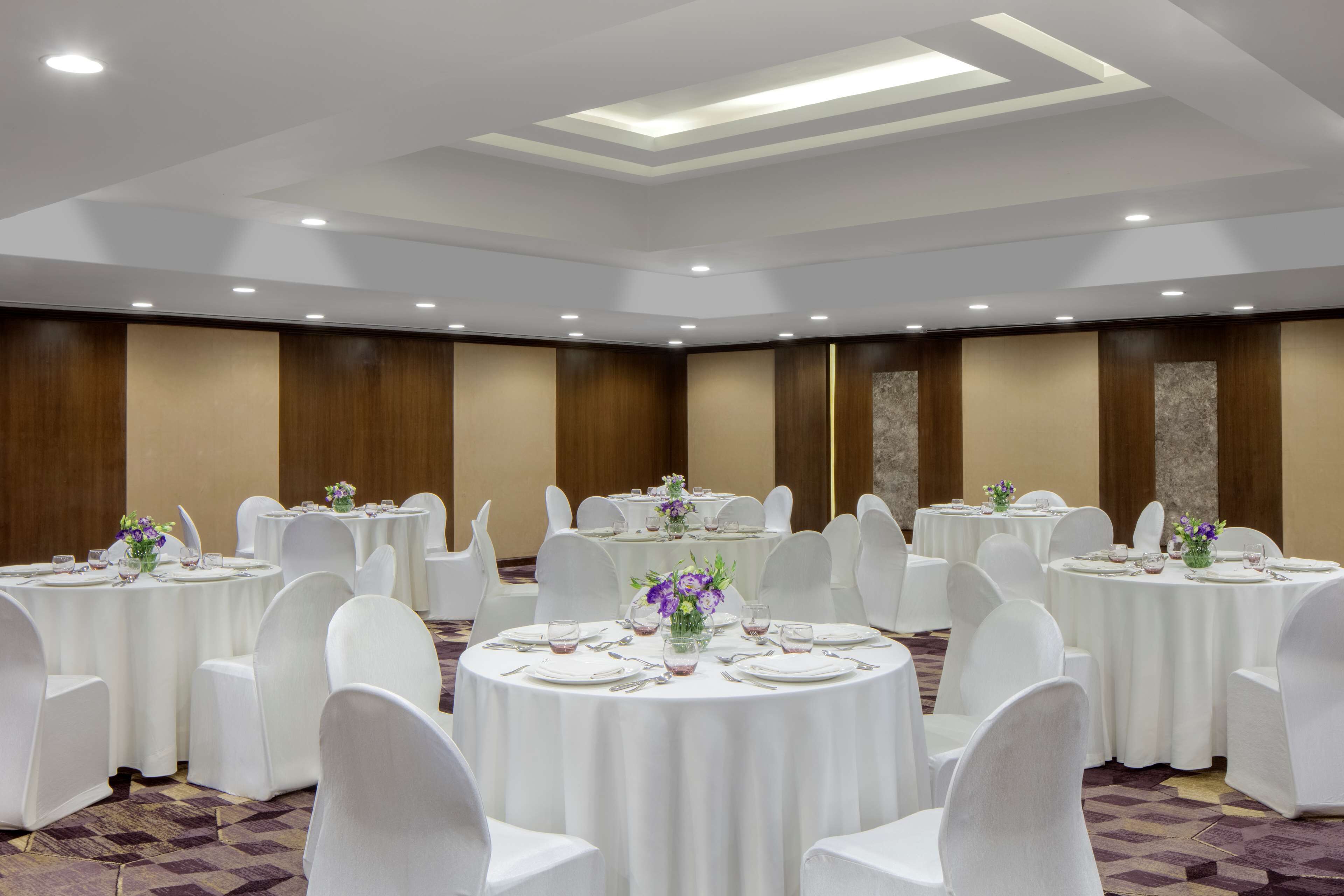 Un salón de banquetes con varias mesas redondas, sillas blancas y centros de mesa florales.