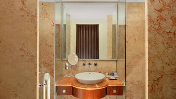 A bathroom with a marble sink, a mirror, and a glass shower enclosure.
