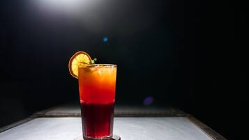 Un vaso de bebida roja adornado con una rodaja de naranja, sobre un posavasos.