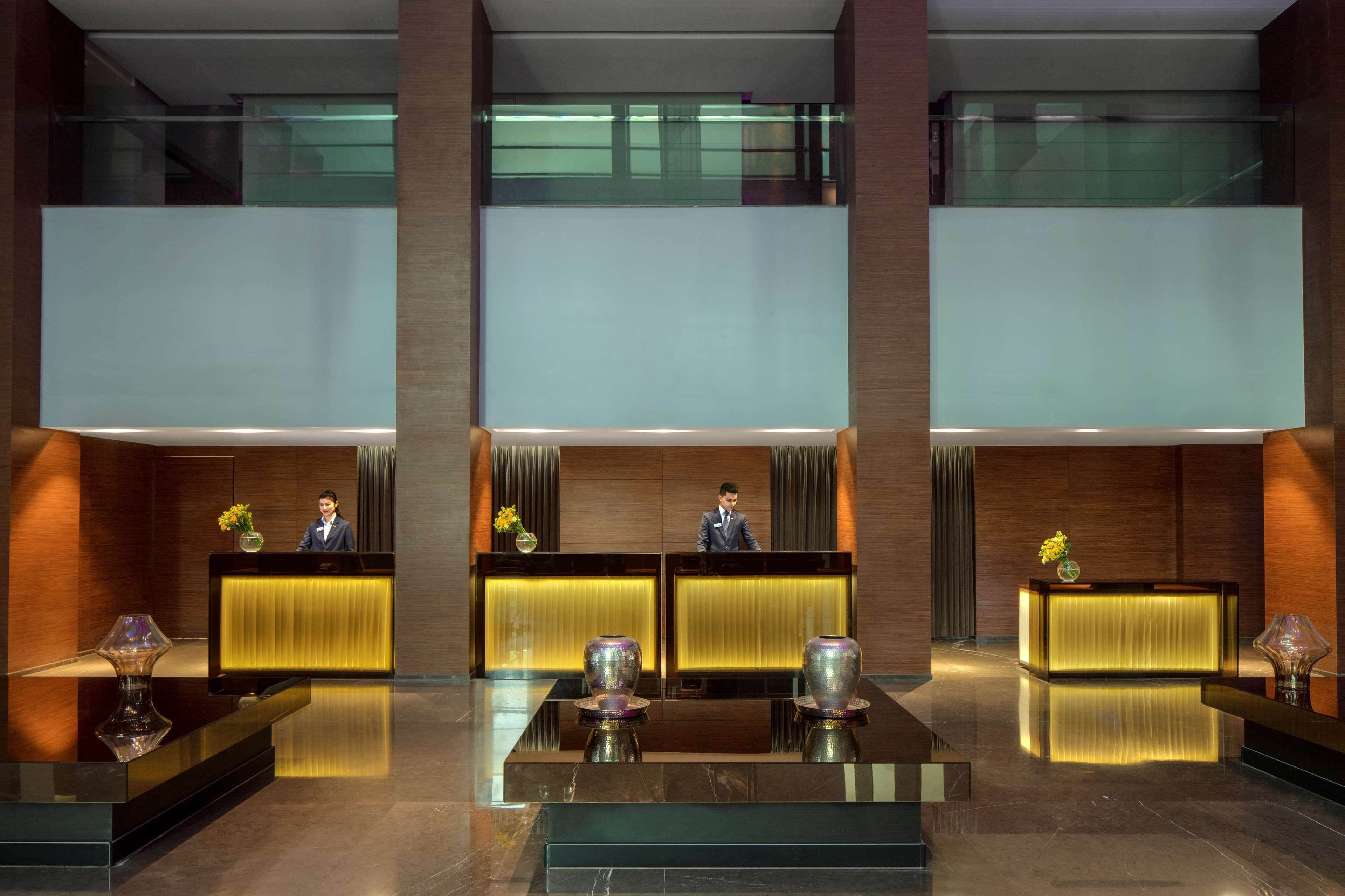 A modern hotel lobby with a reception desk, two large vases, and a polished marble floor.