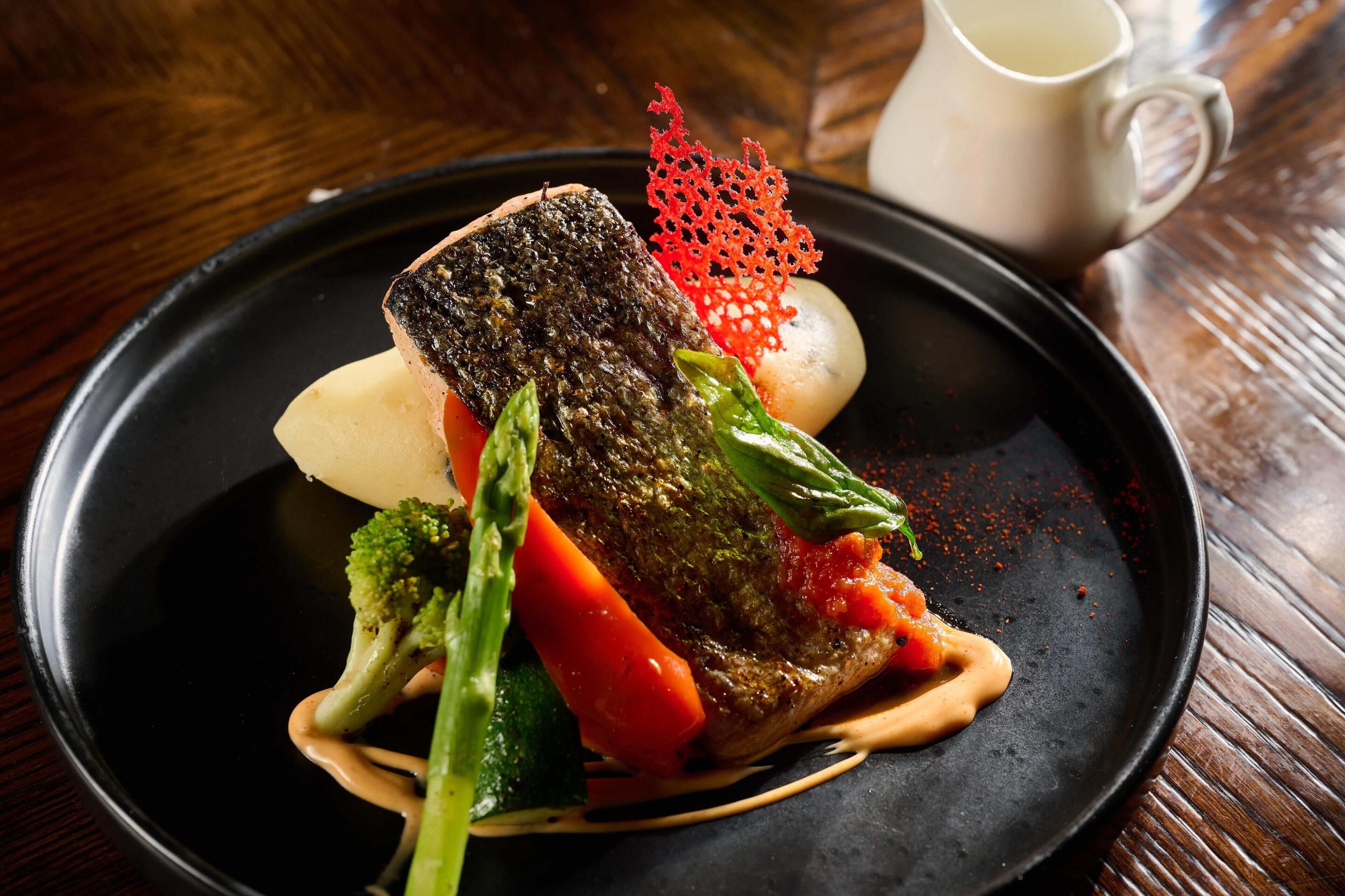 A plate of food with a fish, vegetables, and sauce.